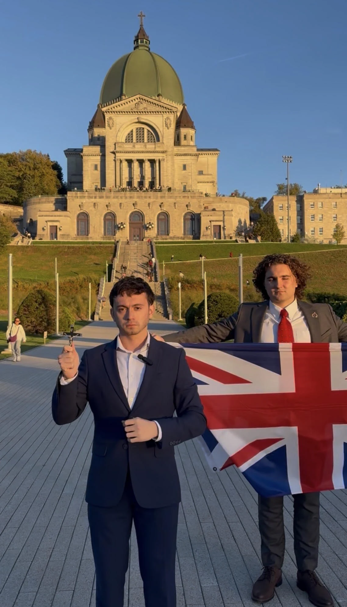 Justice in a blue suit holding a cross, with a British flag and church behind him