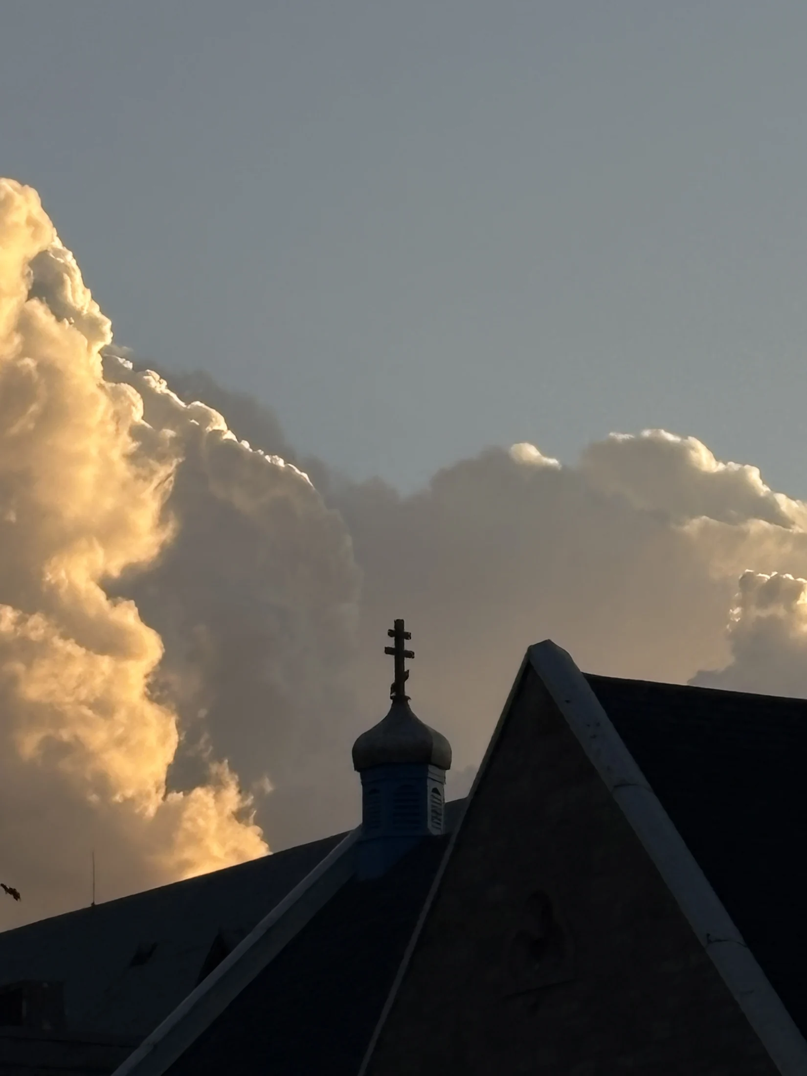 Church roof and cross against a golden evening sky